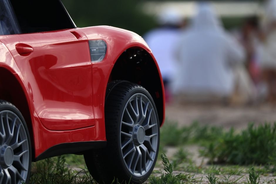 Raudonas žaislinis automobilis ant žolės, simbolizuojantis linksmybes vaikų aikštelėse