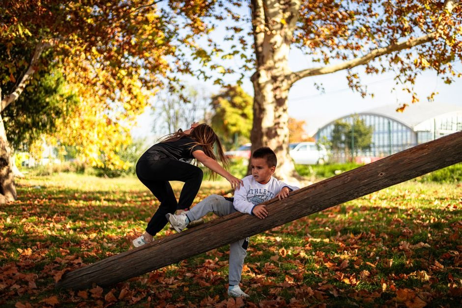 Vaikai džiaugiasi žaidimu ant sūpynių rudens parke, pilname spalvotų lapų
